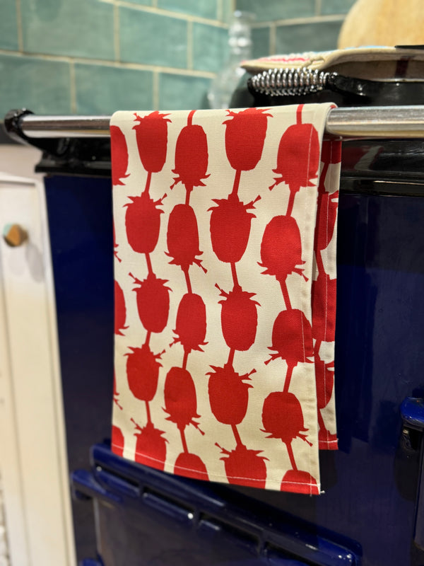 Red and white patterned towel hanging on a stove handle with a green tiled wall in the background.