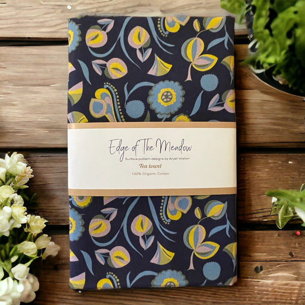 A navy blue tea towel with a colorful floral folk print pattern, laid flat on a wooden surface 